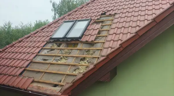 Uszkodzony dach z dachówką, widoczne okna dachowe i izolacja. Czas pomyśleć, jak uszczelnić dach przed kunami.