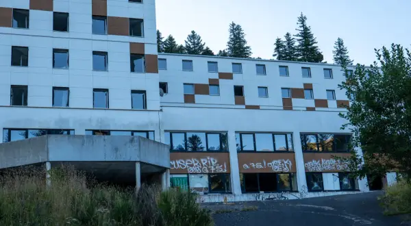 Bâtiment abandonné tagué, vestige d'urbex près du Puy de Dôme. La nature reprend ses droits, fenêtres brisées et végétation envahissante.