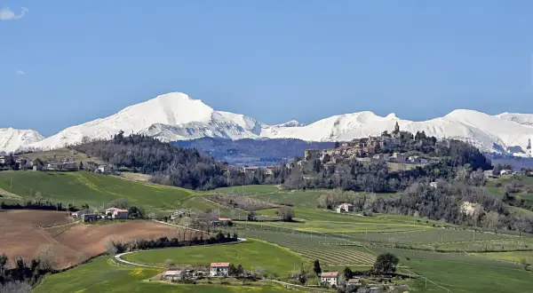 Paesaggio collinare con un borgo in cima, montagne innevate sullo sfondo. Un tranquillo scorcio del fermo provincia.