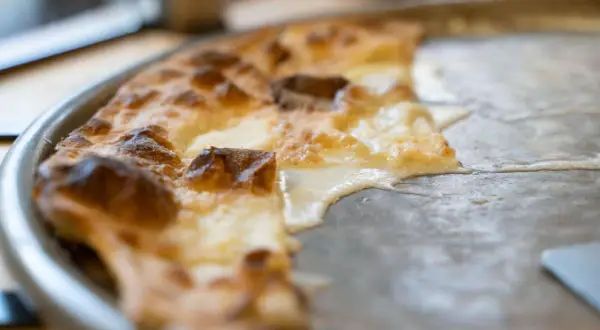 En bit av en gyllene focaccia di Recco med smält ost som rinner ut på en plåt.