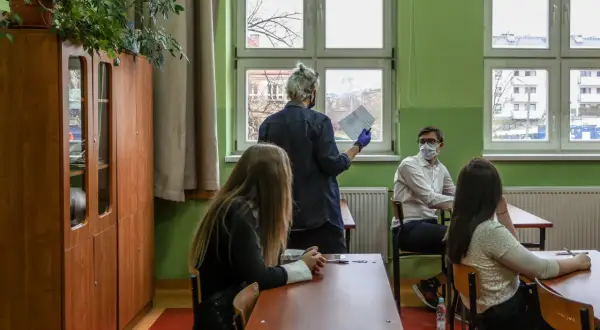 Nauczyciel dyplomowany zarobki - lekcja w klasie, uczniowie siedzą przy ławkach, nauczyciel stoi przy oknie z dokumentami.