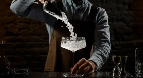 Barman aggiunge ghiaccio tritato in un calice. La corretta temperatura frigo bar bevande è fondamentale per un cocktail perfetto.