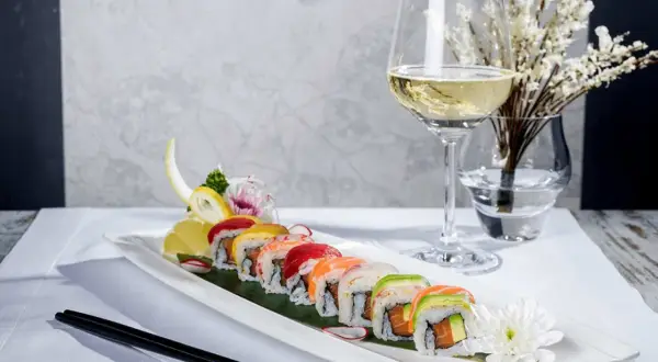 En elegant uppsättning sushirullar med färgglada toppingar, serverade med en glas vin till sushi. En vacker dukning med blommor och ätpinnar.