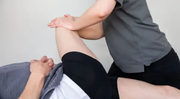 Fysioterapeut utför piriformis behandling genom att massera och stretcha en patients höft.