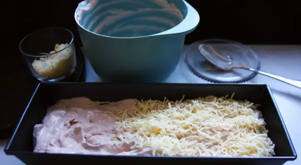 Förberedelser för ett gott kassler recept: en form med kassler och ost, en skål med riven ost och en tom blandskål.