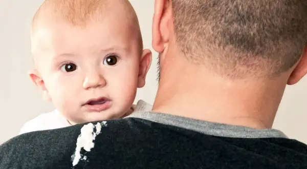 En bebis med stora ögon tittar fram över pappans axel, som har fått en kladdig fläck.