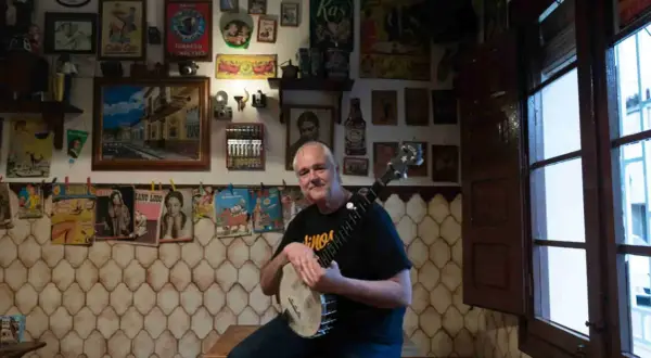 Un hombre sonriente con un banjo en salsipuedes una tasca encantadora, rodeado de carteles vintage y objetos curiosos.