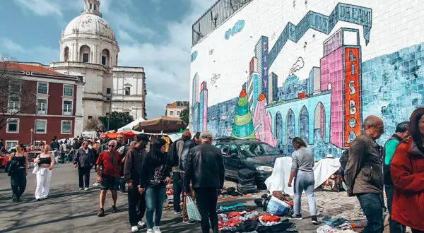 Bunter Flohmarkt in Lissabon mit Menschen, Kuppelkirche und Graffiti-Wand. Hier finden Sie echte Lissabon Geheimtipps.