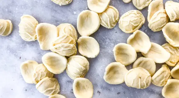 Orecchiette, die "kleinen Ohren" der Pasta, liegen auf grauem Marmor. Die Aussprache ist einfach: Oh-reck-ee-ette.