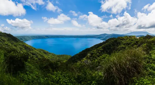 Vista panorámica de un lago azul intenso rodeado de vegetación exuberante y montañas. Un destino imperdible que ver en Nicaragua.
