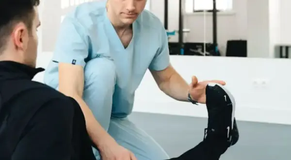 Fizjoterapeuta w jasnoniebieskim uniformie pomaga pacjentowi w ćwiczeniach rehabilitacyjnych.
