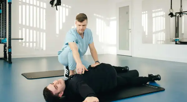 Un kinésithérapeute aide un patient allongé sur un tapis à réaliser un mouvement pour le diagnostic du syndrome du piriforme.