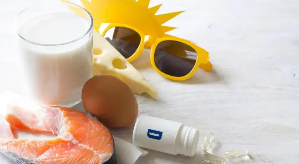Zomerse zon, zonnebril en voedingsmiddelen die een stootkuur vitamine D bieden: zalm, ei, melk en kaas. Ook supplementen zijn zichtbaar.