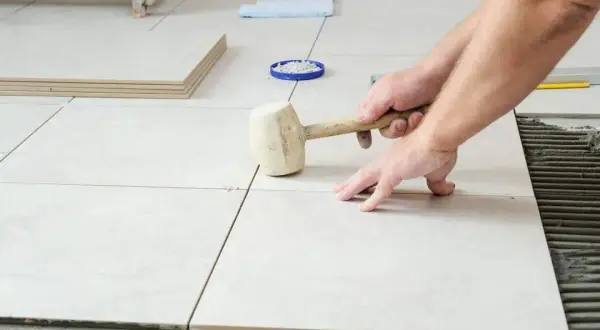 Pose de carrelage sans plinthe, un artisan ajuste une dalle avec un maillet en caoutchouc sur le mortier frais.