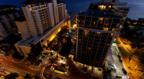 Wieczorem widać kompleks condo hotel z basenem i palmami. Światła budynków i ulic tworzą ciepłą atmosferę.