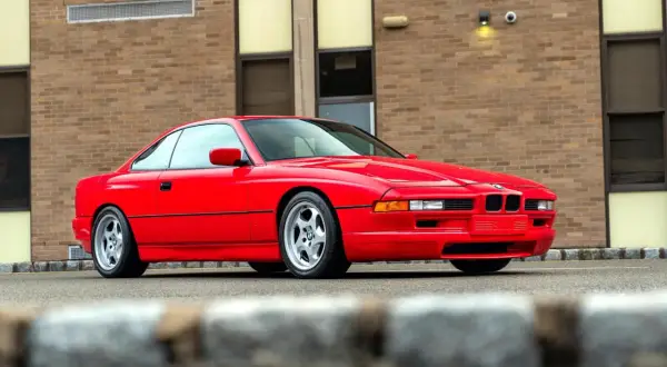 Czerwone BMW serii 8 (E50) z lat 90. zaparkowane przed budynkiem z cegły.