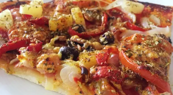 En bit pizza med ananas, oliver och paprika. Ett perfekt glutenfri pizzadeg recept för en god middag.