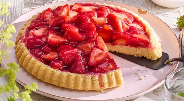 Ein saftiger Erdbeerkuchen, frisch belegt mit vielen roten Erdbeeren und glänzendem Tortenguss. Ein Stück ist bereits herausgeschnitten.