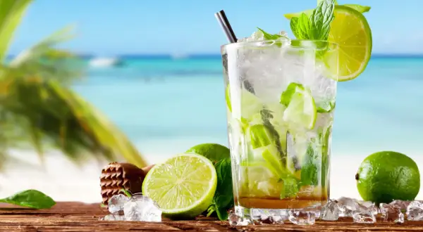 Orzeźwiający mohito czy mojito na plaży? Szklanka pełna lodu, mięty i limonki, z widokiem na turkusowe morze i palmę.