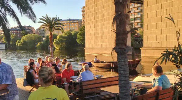 Folk njuter av kvällen vid loopen Hornstull. En båt glider förbi i vattnet.