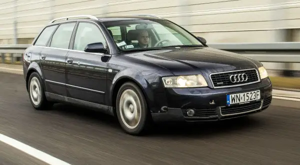 Ciemnogranatowe Audi B6 Avant pędzi autostradą. Kierowca skupiony na drodze.