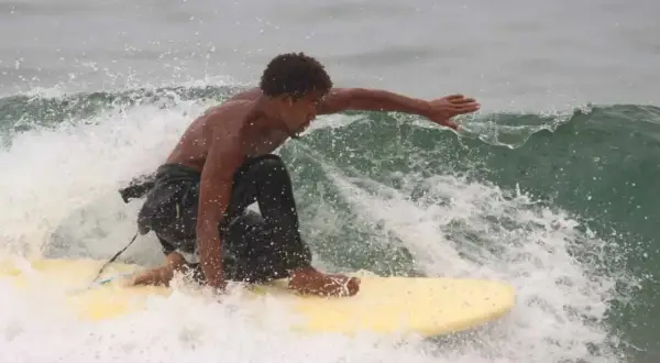 Un jeune homme surfe sur une vague à Tamraght, éclaboussant d'eau.