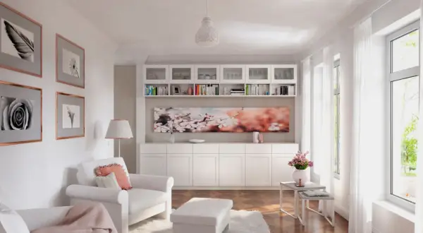 Ein helles, kleines Zimmer mit weißen Möbeln, Bücherregalen, Kunstwerken und einem großen Fenster.