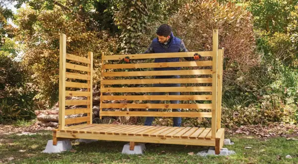 Uomo in piedi davanti a una nuova legnaia in legno, pronta per accogliere la legna per l'inverno.