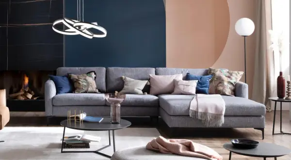 Ein hellgraues Sofa dekorieren mit Kissen in Rosa, Blau und floralen Mustern. Eine Decke liegt darüber.