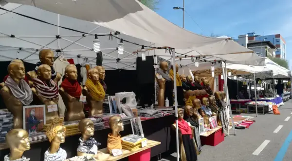 Bancarelle colorate alla fiera di Fano, con manichini dorati che indossano sciarpe e foulard.