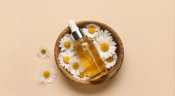 Flacon d'huile dorée entouré de marguerites dans un bol en bois. Le bisabolol, ingrédient clé, promet des bienfaits apaisants.