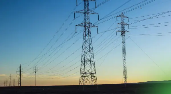 Wieże energetyczne niosące prąd przemienny na tle zachodzącego słońca.