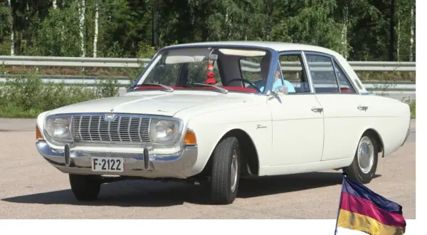 Vit Ford Taunus, en klassisk modell av svenska bilar, parkerad utomhus med en tysk flagga i förgrunden.