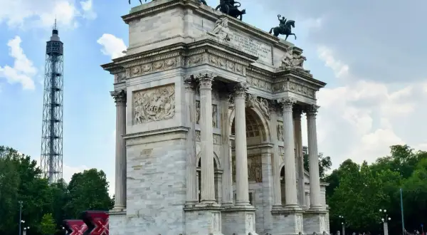 Arco di Pace a Milano, con la torre bianca sullo sfondo e un cielo nuvoloso.