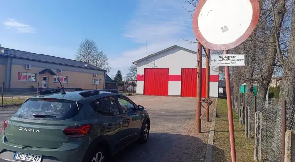 Zielony Dacia Sandero zaparkowany przy remizie OSP. Znak zakazu wjazdu, który nie dotyczy pojazdów OSP, może sugerować mandat za wjazd pod zakaz.
