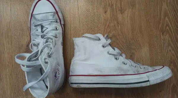 Białe trampki na drewnianym tle. Pokazują, jak wiązać trampki, z luźno zwisającymi sznurówkami.