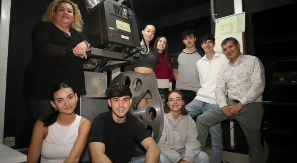 Grupo de jóvenes y adultos posan junto a un proyector antiguo en el cine Cerbuna de Zaragoza.