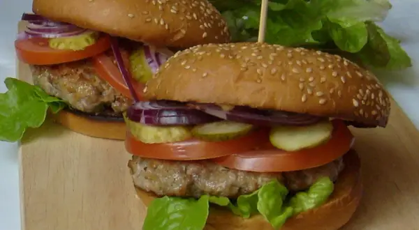 Dwa soczyste burgery z bułkami do hamburgerów pysznie czy przepysznie, z pomidorami, ogórkami, cebulą i sałatą.