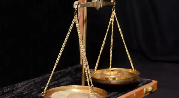 Waga szalkowa z monetami i ciężarkami. Na jednej szalce leżą monety, na drugiej ciężarki, symbolizujące uncję złota.