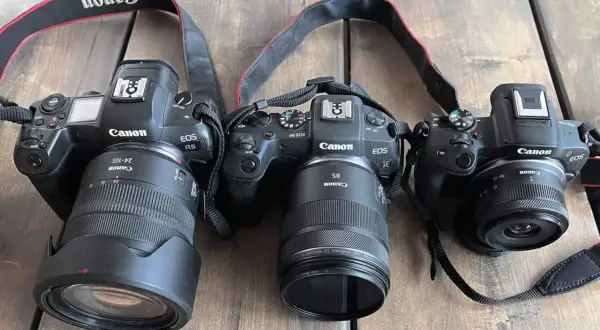 Trzy aparaty Canon EOS R z obiektywami. Jeden z nich, Canon EOS R5, ma obiektyw 24-105mm. Kolejny, Canon EOS RP, wyposażony jest w obiektyw 85mm. Najmniejszy aparat, Canon EOS R50, posiada obiektyw 18-45mm. Wszystkie aparaty mają matrycę APS-C.