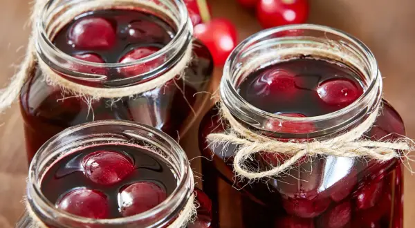 Drei Gläser mit saftigen sauerkirschen einkochen, mit Juteband verziert, bereit für den Winter.