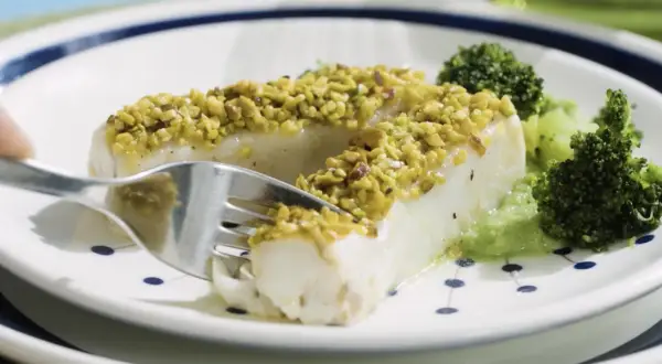 Filetti di merluzzo surgelati, impanati con pistacchi croccanti, serviti con broccoli e una salsa verde.