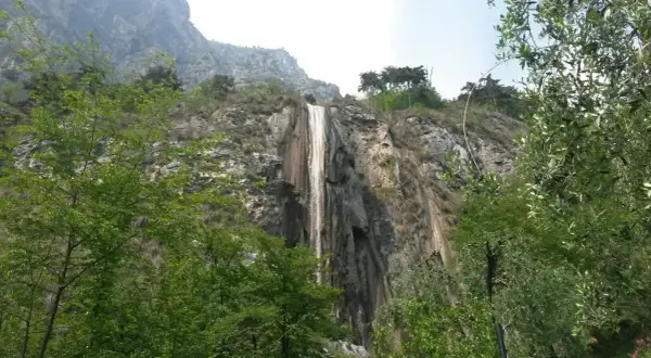 Cascata del Sopino, un velo d'acqua scende da una parete rocciosa circondata da vegetazione lussureggiante.