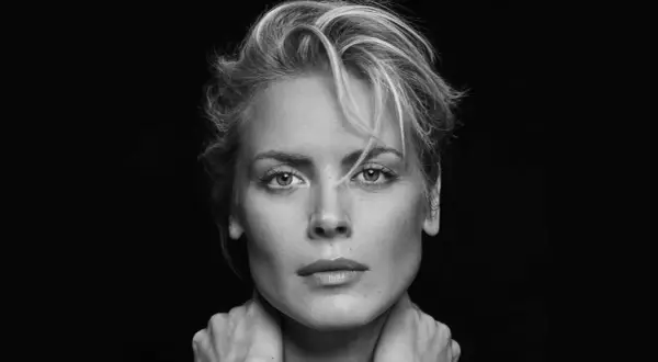 Synnøve Macody Lund, mit ihrem markanten Blick und den Händen am Hals, posiert in einem dramatischen Schwarz-Weiß-Porträt.