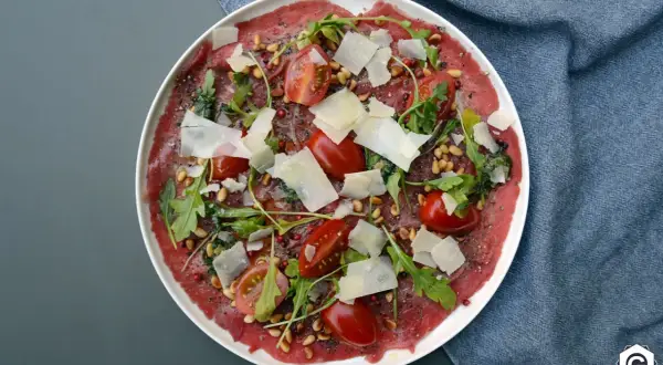 Carpaccio de bœuf finement tranché, garni de tomates cerises, roquette, pignons de pin et copeaux de parmesan. Un délice visuel et gustatif.