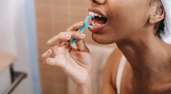 Mujer usa hilo dental, evitando errores al cepillarse los dientes.