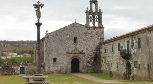 El monasterio de Aciveiro, con su iglesia de piedra y campanario, se alza majestuoso. Un cruceiro antiguo preside el patio.