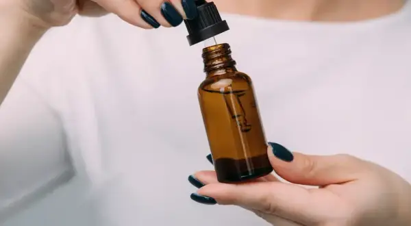 Dłonie z ciemnym lakierem do paznokci trzymają brązową buteleczkę z pipetką. Czy serum do twarzy można stosować codziennie?