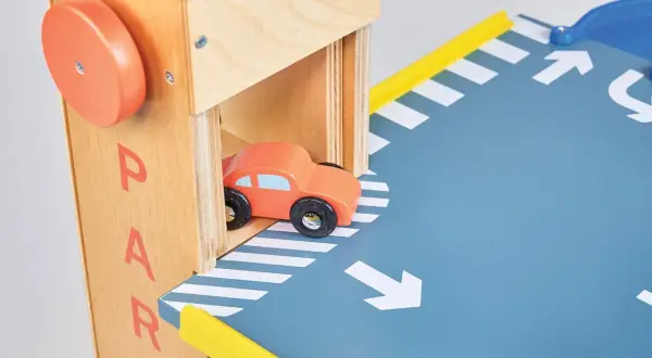 Drewniany parking na autka z pomarańczowym samochodzikiem wjeżdżającym na rampę.