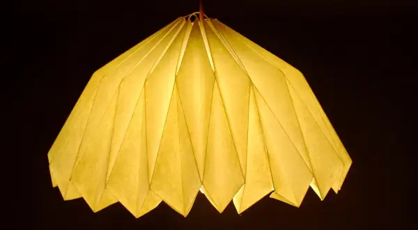 Oświetlony, żółty abażur z papieru, złożony jak origami. Inspiracja, jak zrobić abażur z papieru, dla Twojego wnętrza.